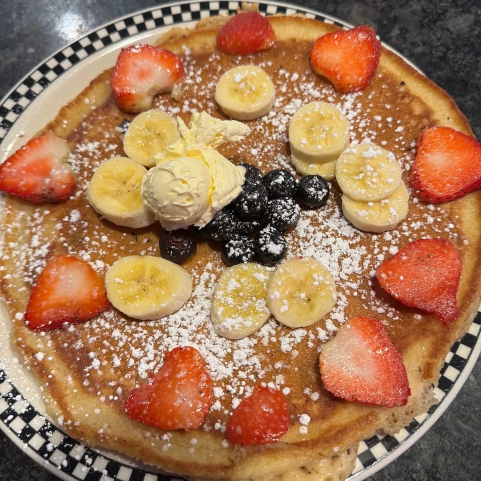 A large pancake topped with strawberries, bananas, blueberries, butter, and powdered sugar.